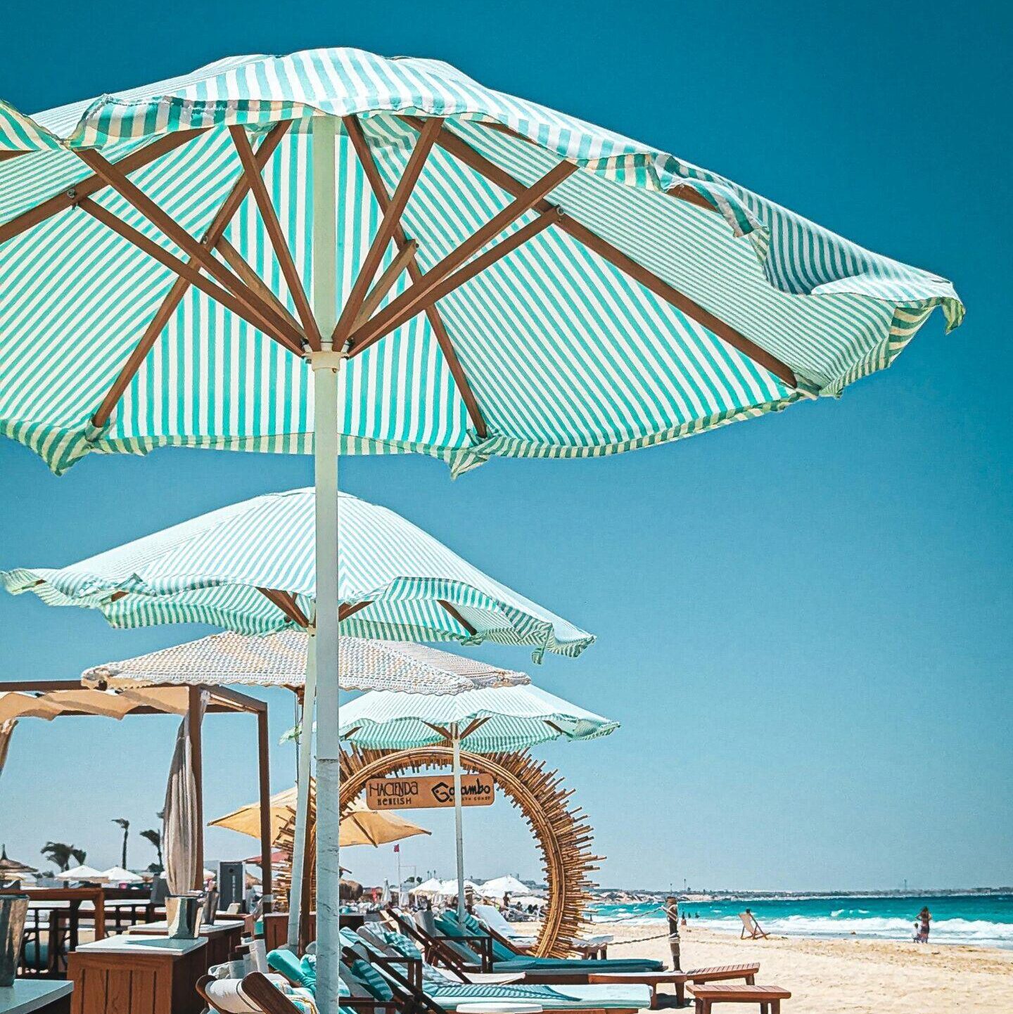 A relaxing sunny beach scene with lounge chairs and striped umbrellas by the ocean.